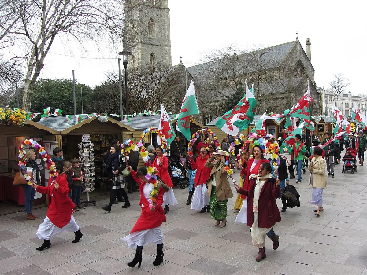 Marchers in red capes carrying Welsh dragon flags and garlands of daffodils parade down a shopping street in Cardiff