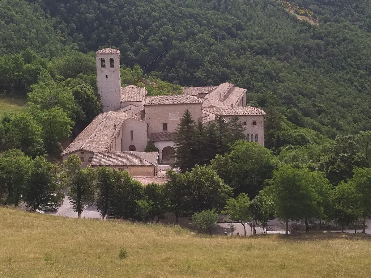 The stone monastery of Fonte Avellana with its bell tower on a green wooded slope of Monte Catria