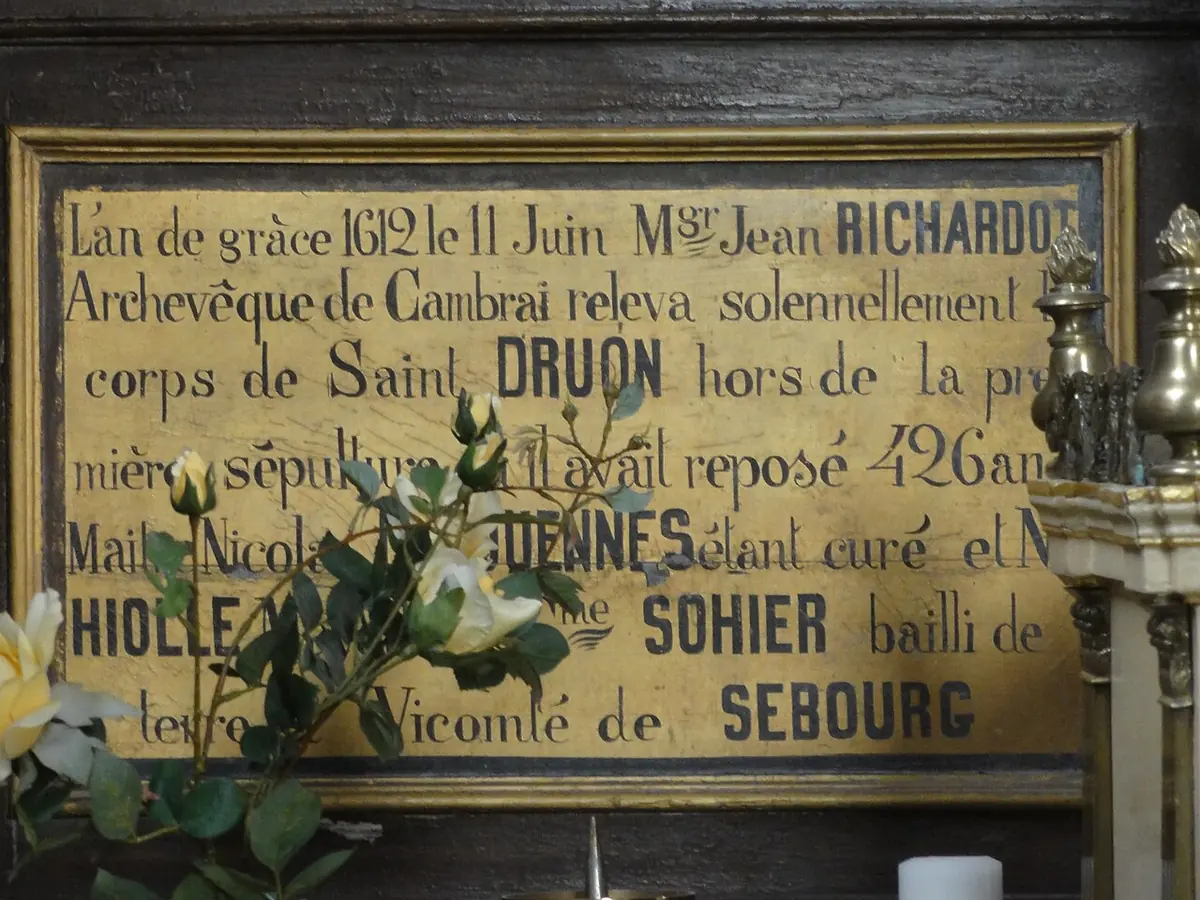 A gold-painted plaque in a dark wooden frame recording in French that on June 11, 1612, Archbishop Jean Richardot of Cambrai solemnly raised the body of Saint Druon after 426 years in its first grave