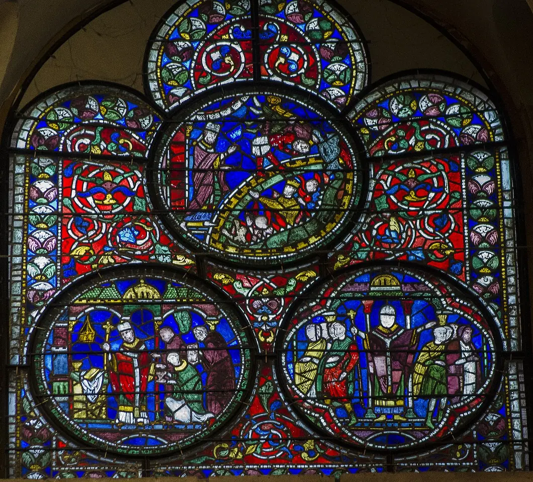 Medieval stained-glass window of three round medallions in deep blue and red showing scenes from the life of St. Dunstan