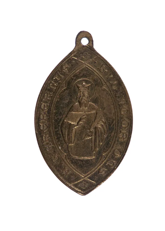 A small oval devotional medal in worn silver-colored metal with a loop at the top, showing a standing saint surrounded by a Dutch inscription