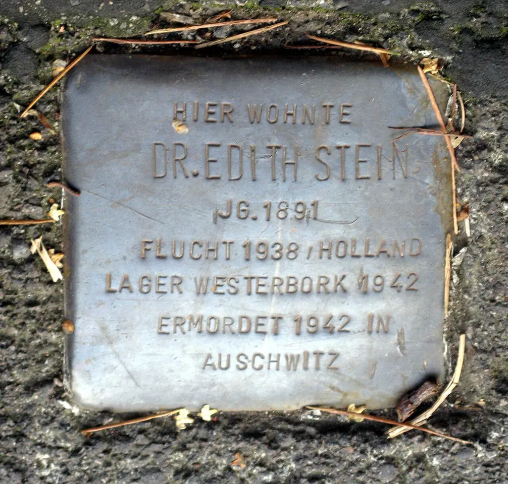 A small brass paving stone set in the ground, engraved in German with Edith Stein's name, her birth year, her flight to Holland in 1938, Westerbork camp and her murder at Auschwitz in 1942