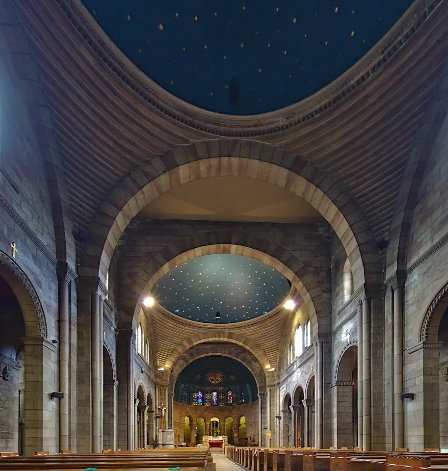 A long stone nave with round arches and domed ceilings painted dark blue with gold stars, leading to a lit altar