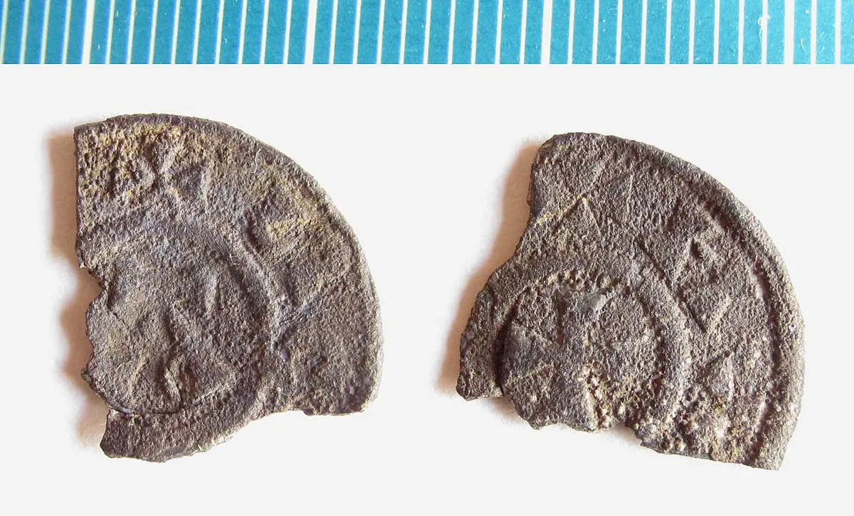 Two sides of a broken, worn silver penny with a cross in a circle and traces of lettering, beside a measuring scale