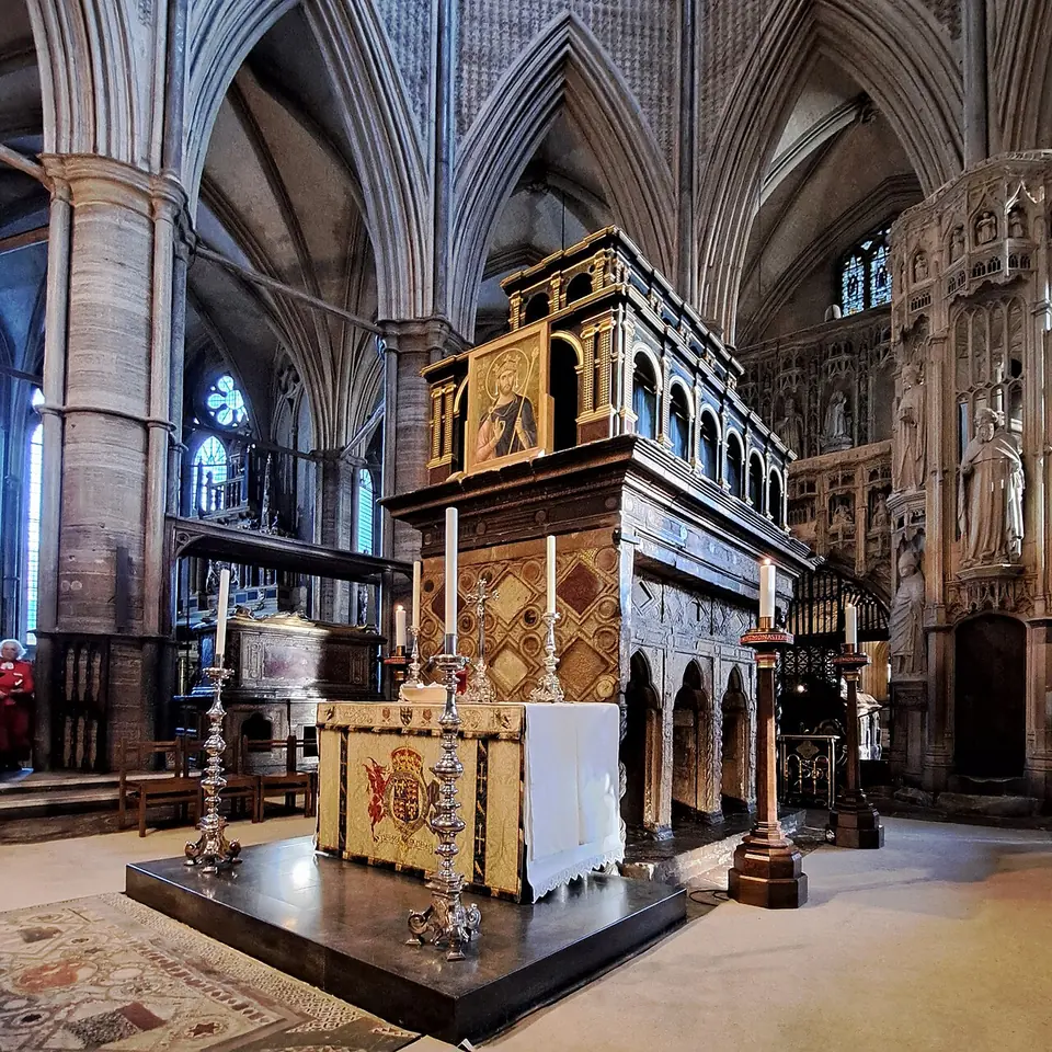 The tall stone shrine of St. Edward with its wooden upper canopy and recesses in its base, behind an altar with candlesticks in a Gothic chapel