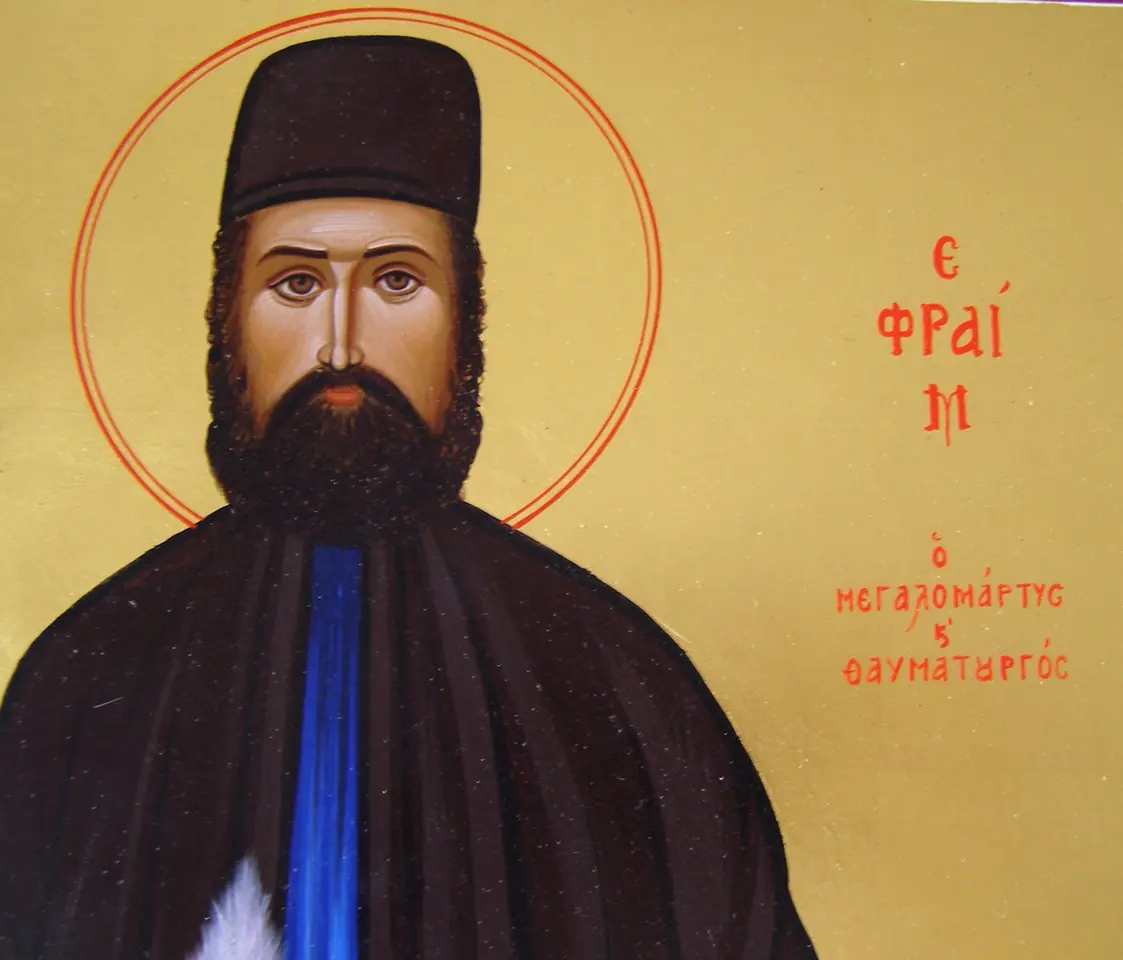 Detail of a Greek icon of St. Efraim with a black beard and black monastic cap on a gold background, with his name and the title Great Martyr and Wonderworker in red Greek letters