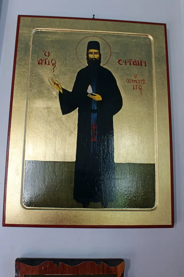 Full-length icon on a gold ground of St. Efraim standing in black monastic robes, holding a small cross and raising his hand