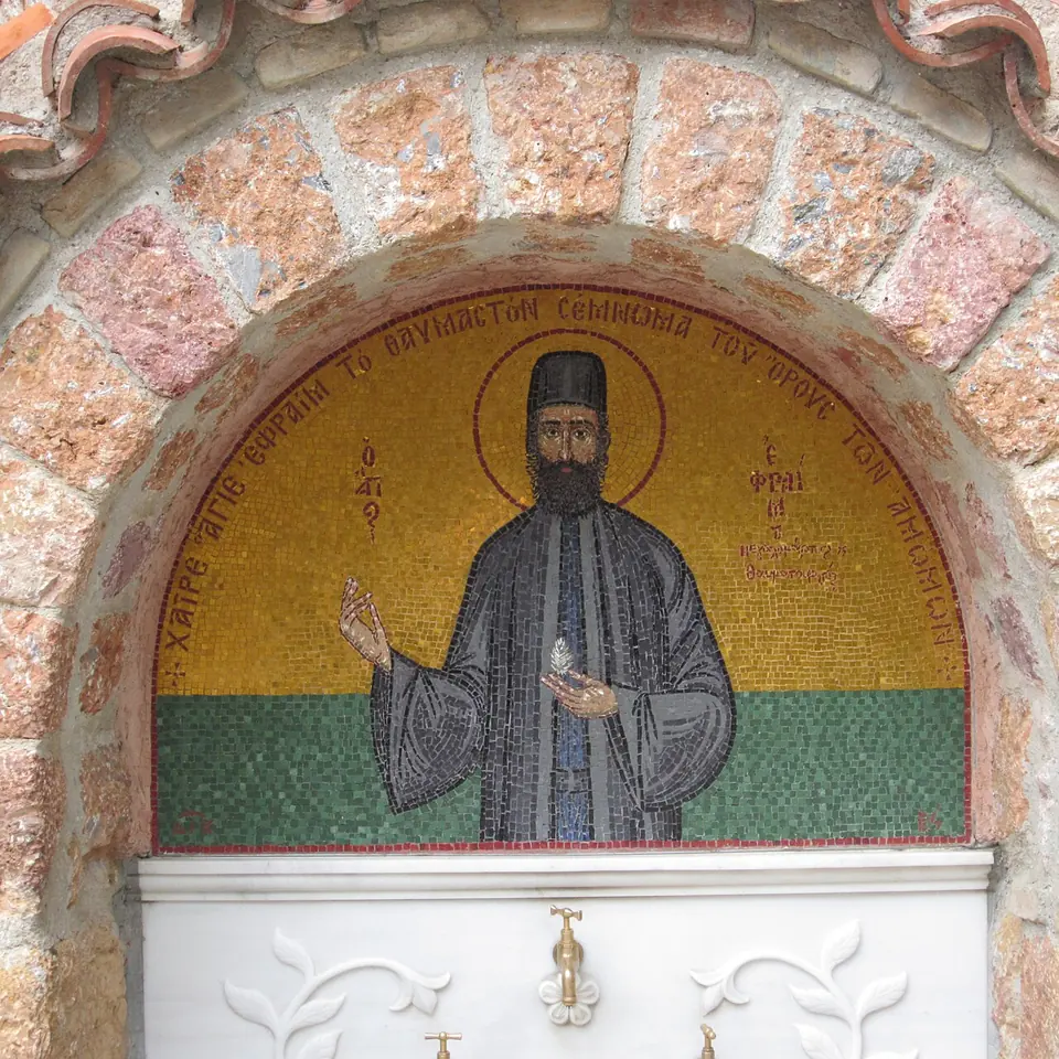 Gold mosaic of St. Efraim in a stone arch above a white marble fountain with brass taps, with a Greek inscription around the arch