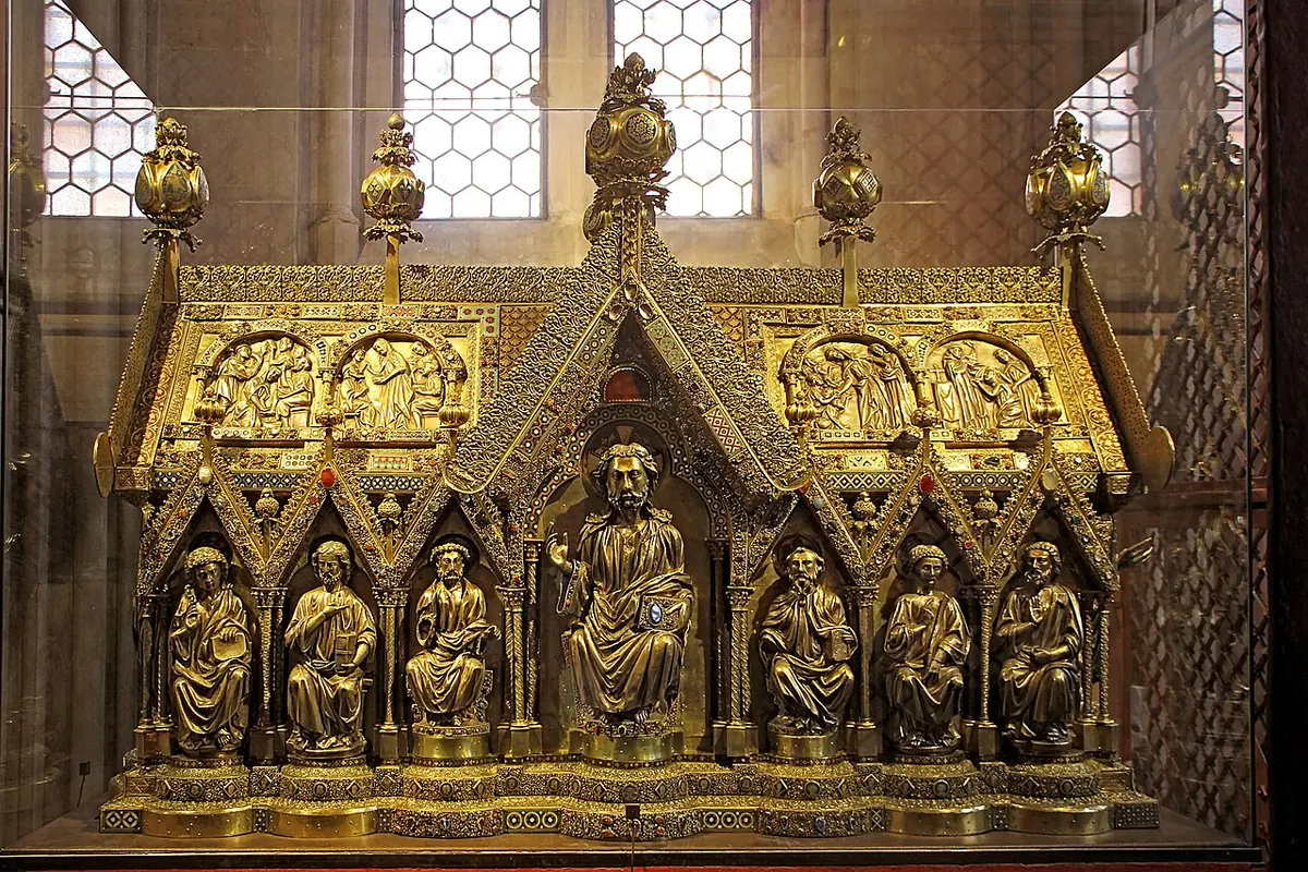 A gilded shrine shaped like a small church with gabled roof and rows of seated apostles in arched niches, behind glass