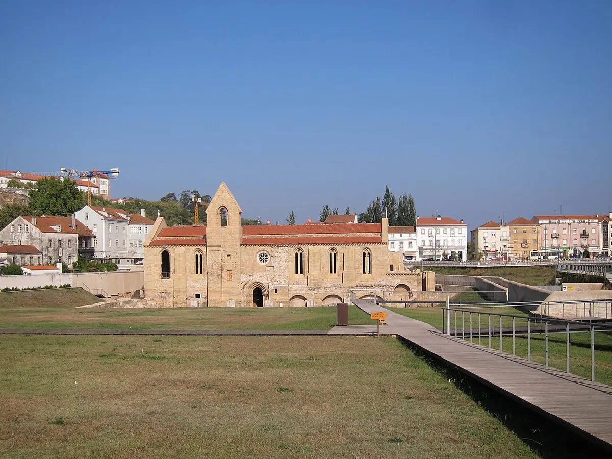 The roofless Gothic church of the old Poor Clare monastery on the low bank of the Mondego River in Coimbra, with the city on the hill behind