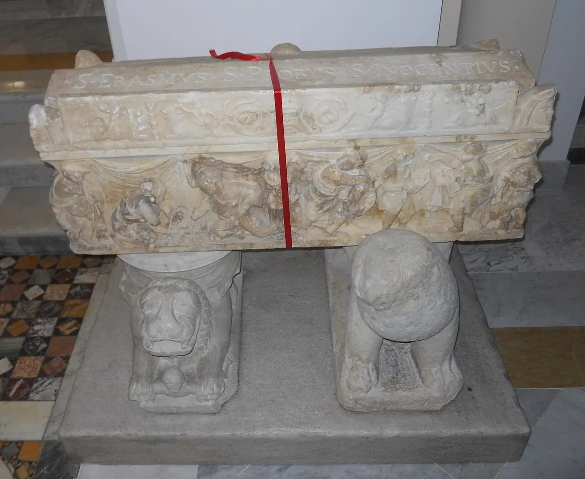 An ancient carved marble sarcophagus resting on two stone lions in Gaeta Cathedral, tied with a red ribbon