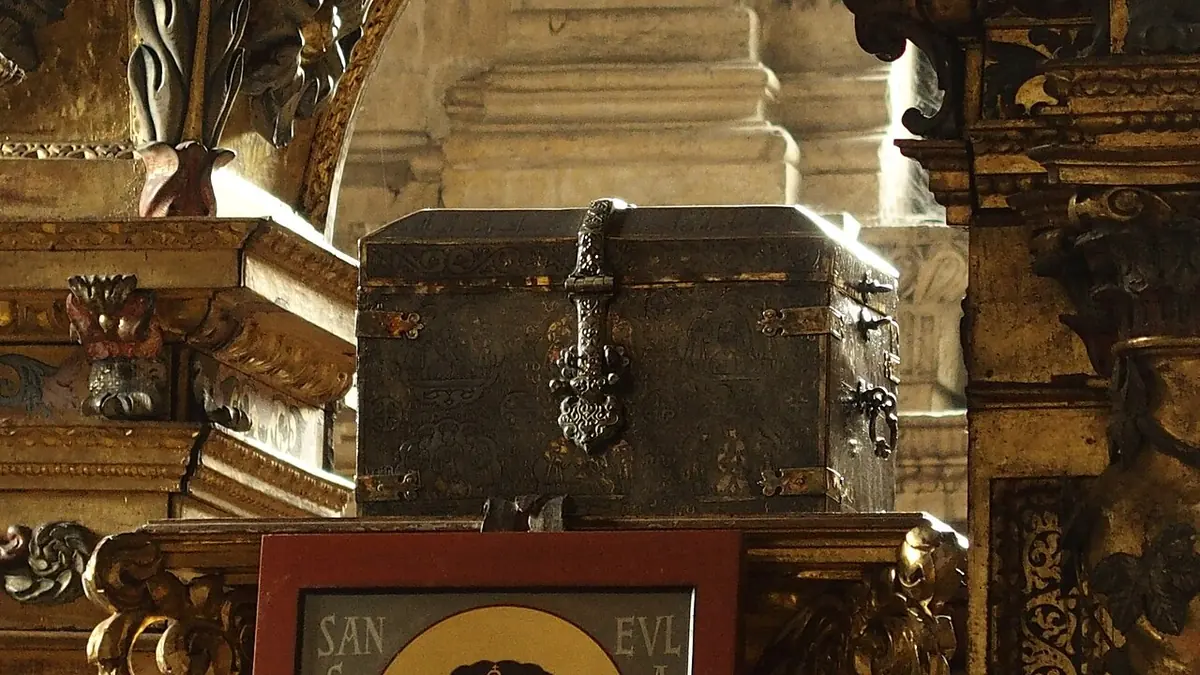 Dark silver casket with a domed lid and ornate fittings resting in a gilded Baroque altarpiece in Oviedo Cathedral, above a small painted panel bearing her name