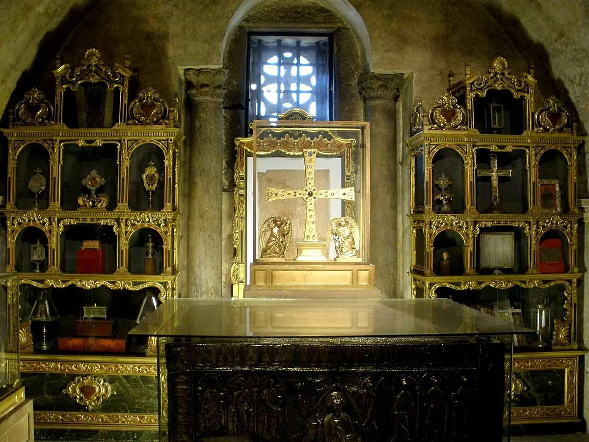 A small vaulted stone chapel with gilded reliquary cabinets on either side and a golden jeweled cross displayed at the far end