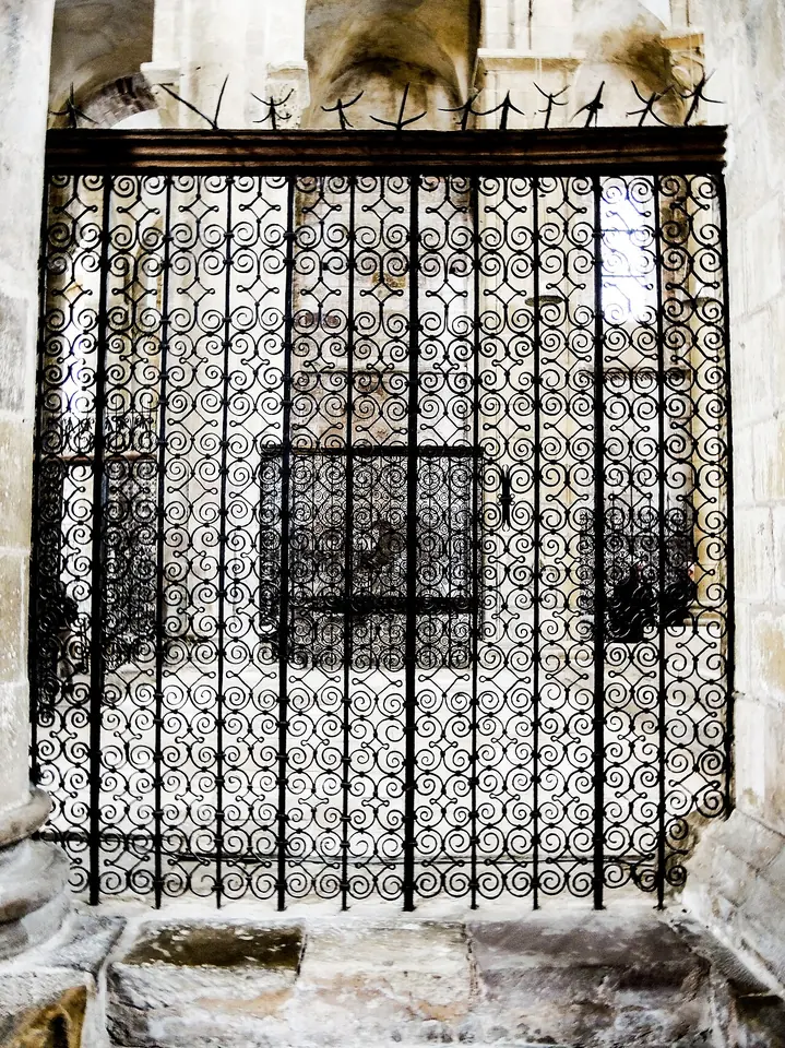 A tall wrought-iron screen of tight spirals and scrolls closing an arch in the choir of the abbey church at Conques