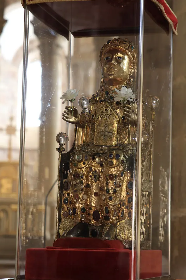 The golden seated reliquary statue of Sainte Foy, covered in gems and cameos, with a crown and raised hands, in a glass case in the abbey church