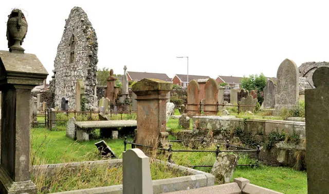 The roofless stone gable of a ruined medieval church rising above an old graveyard full of headstones and tombs