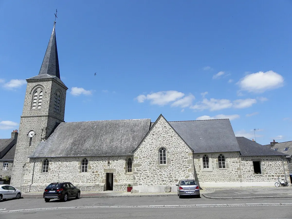 A gray stone village church with a slate roof and a square bell tower topped by a slender spire, on a sunny street