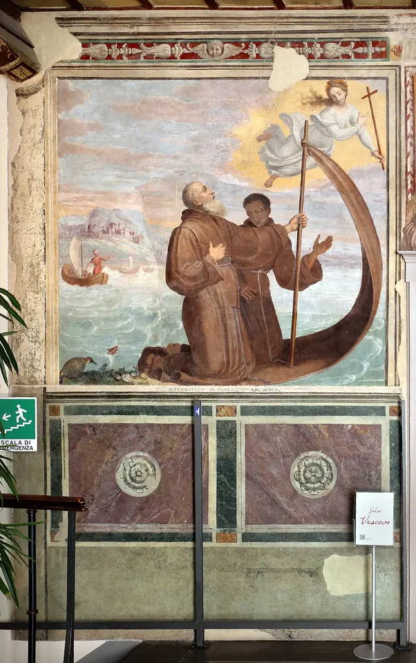 Fresco of two kneeling hermits in brown habits riding a cloak on the waves, its edge raised on a staff like a sail, with an angel above and a city on the shore behind