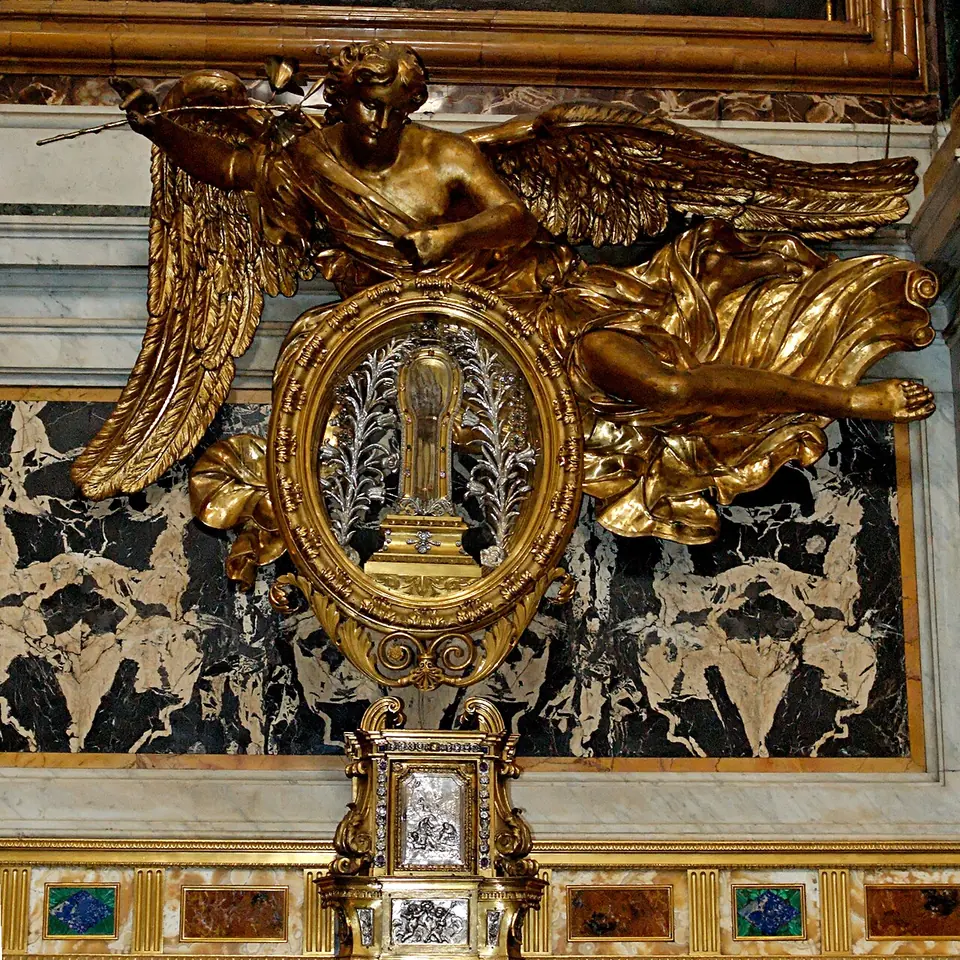 A gilded oval reliquary framed by a golden angel with spread wings, set into a black-and-white marble altar