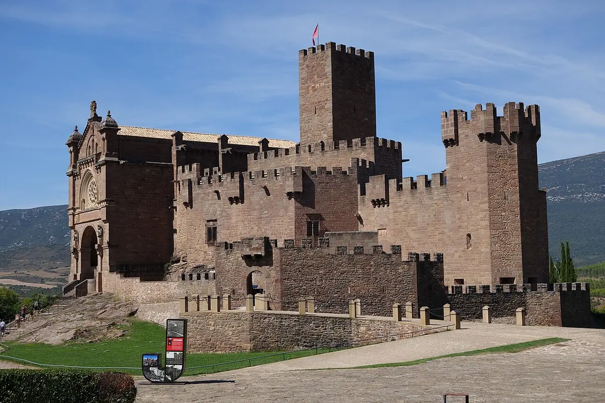 A restored medieval stone castle with square crenellated towers and a church facade beside it, under a blue sky