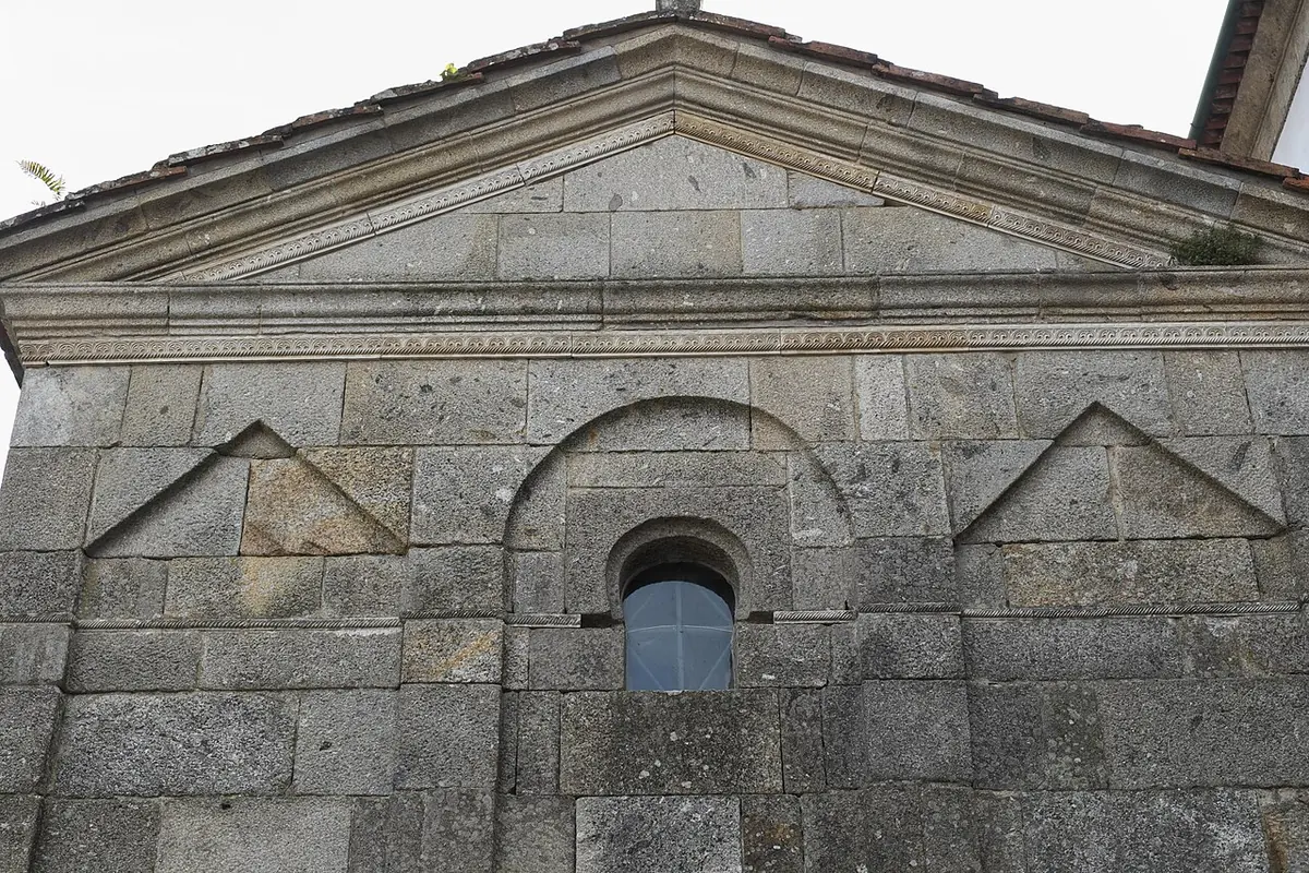 A granite wall of an early medieval chapel decorated with alternating round and pointed blind arches and a small round-headed window