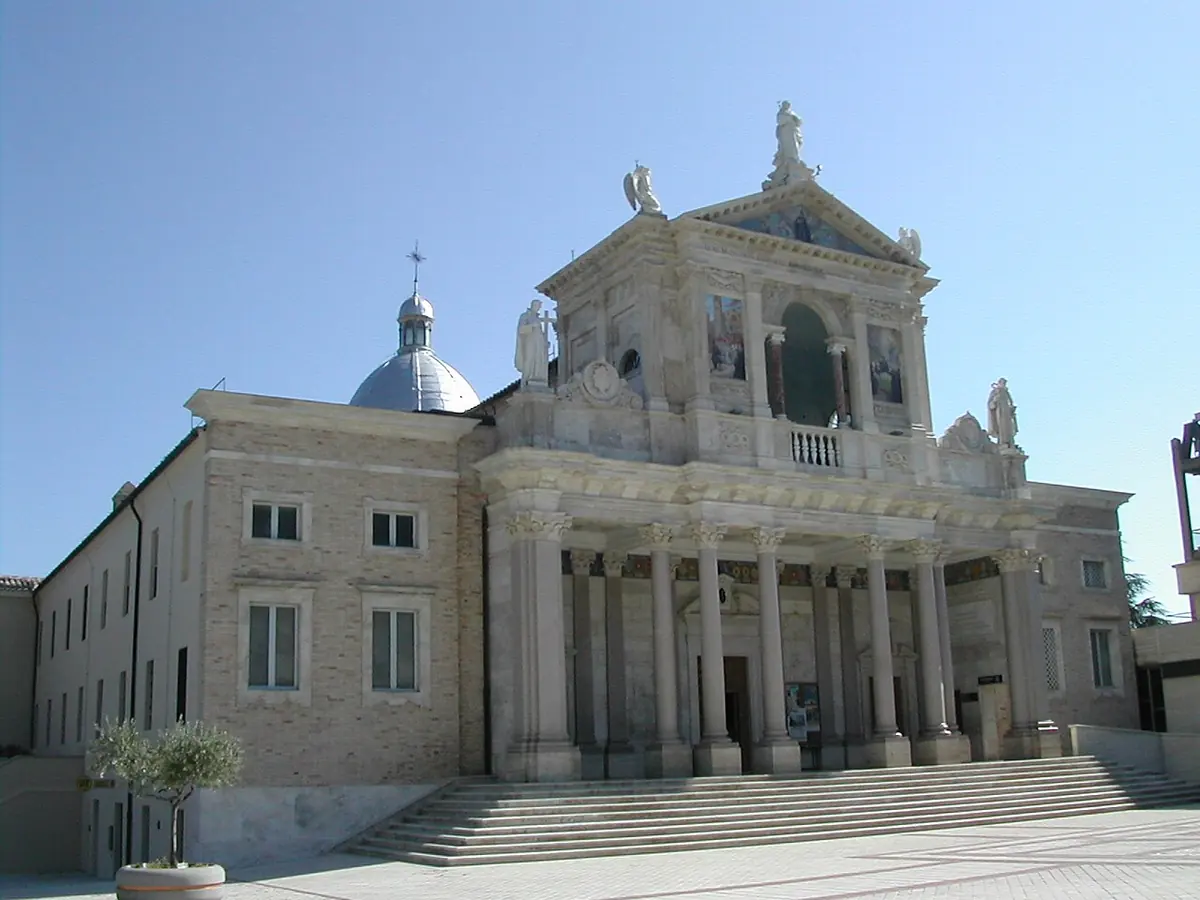 The white neoclassical facade of the old basilica of San Gabriele with columns, statues and a dome, beside the long convent building