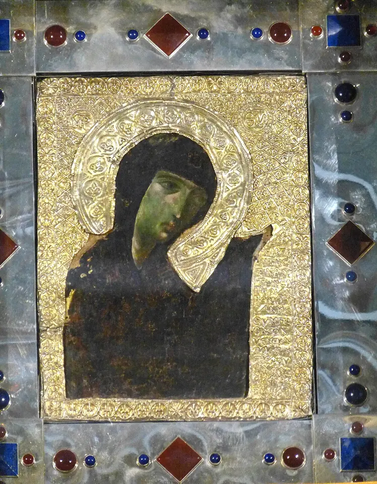 A small dark Byzantine icon of the Virgin Mary's face and veiled head, turned in prayer, set in a gold halo and a silver frame studded with red and blue stones