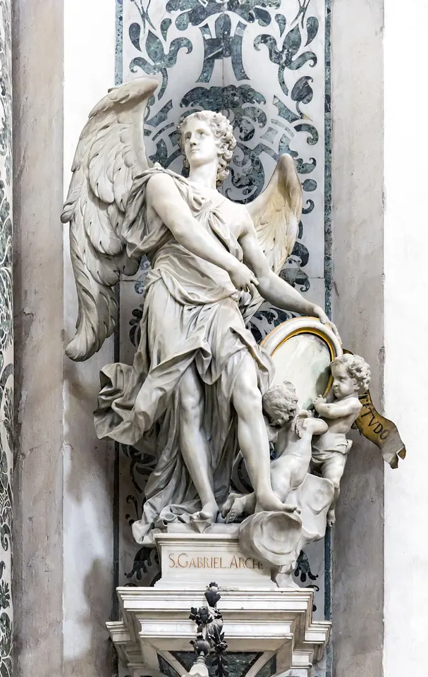 White Baroque marble statue of a winged archangel standing on a pedestal against a wall inlaid with green and white marble, with a small cherub at his feet