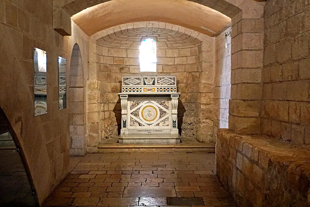 A small white marble altar in a vaulted stone grotto with an arched window, inside the Basilica of the Annunciation in Nazareth