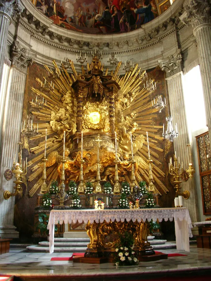 A Baroque high altar with a towering gilded sunburst and angels surrounding a small icon, under a painted dome