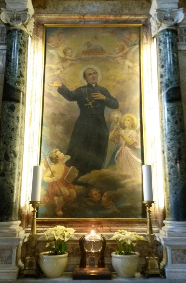 An altar painting framed by dark marble columns showing a priest in a black cassock rising into the clouds among angels, with lilies and a small candle below