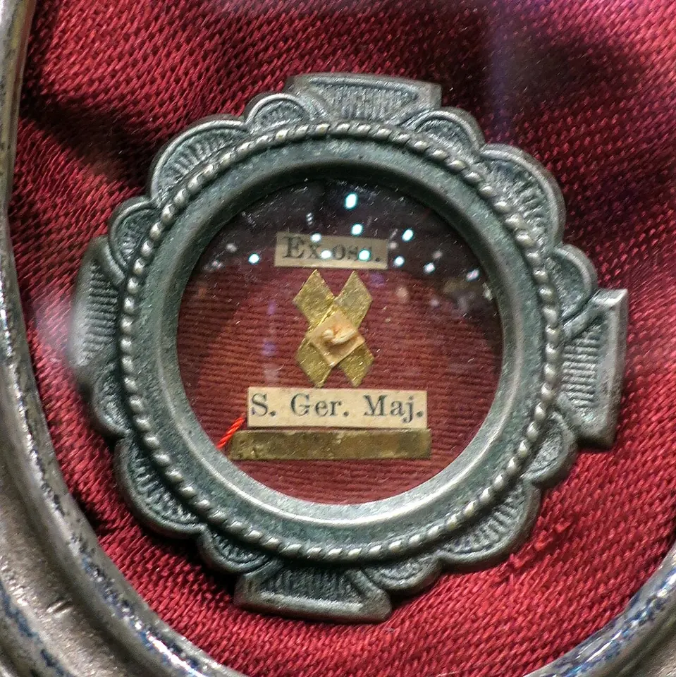 Small round silver reliquary on red silk with a tiny relic behind glass and a paper label reading "S. Ger. Maj."