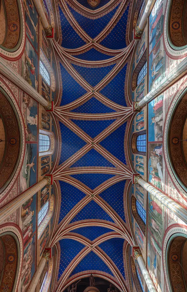 Looking straight up at a Gothic vaulted ceiling painted deep blue with gold stars, its ribs and the walls below covered in red, gold and blue painted patterns