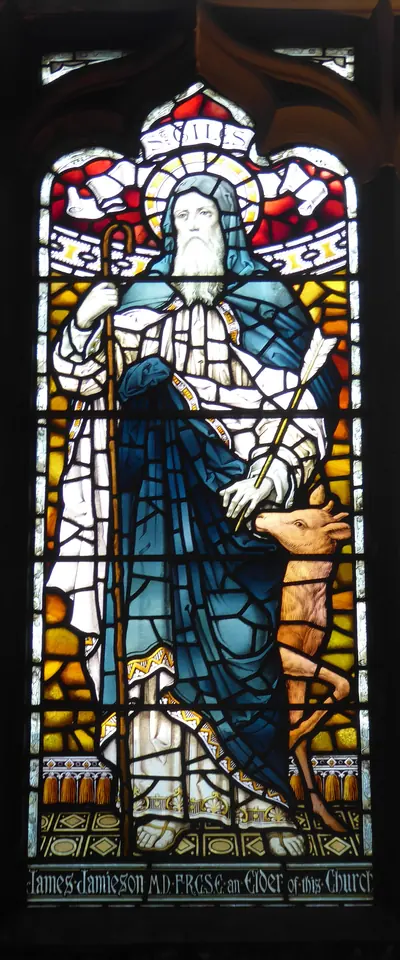 Stained-glass window of a white-bearded hermit in a blue cloak holding a staff, with a small deer at his feet