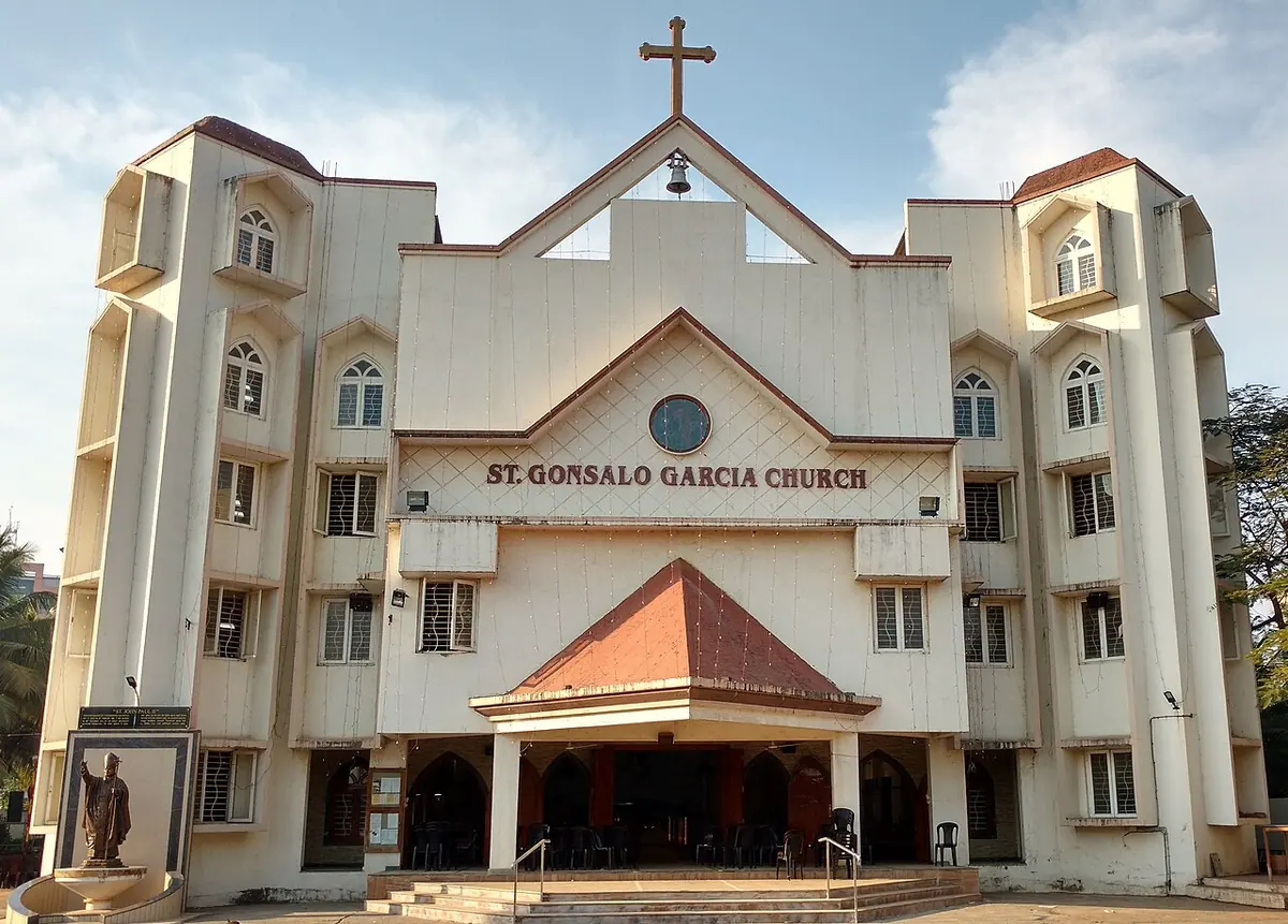 Large modern white church with a cross on its gable, a tiled entrance porch and the name St. Gonsalo Garcia Church on the facade