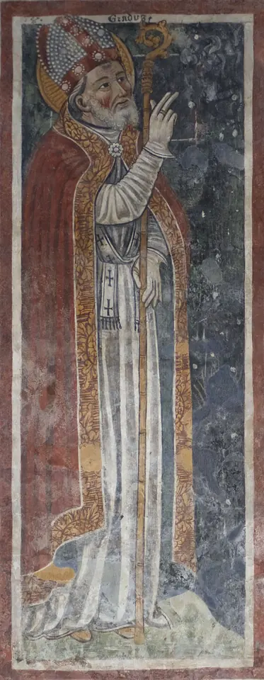 Tall, faded fresco of a white-bearded bishop in a miter and red cope, looking up and raising his hand toward the sky