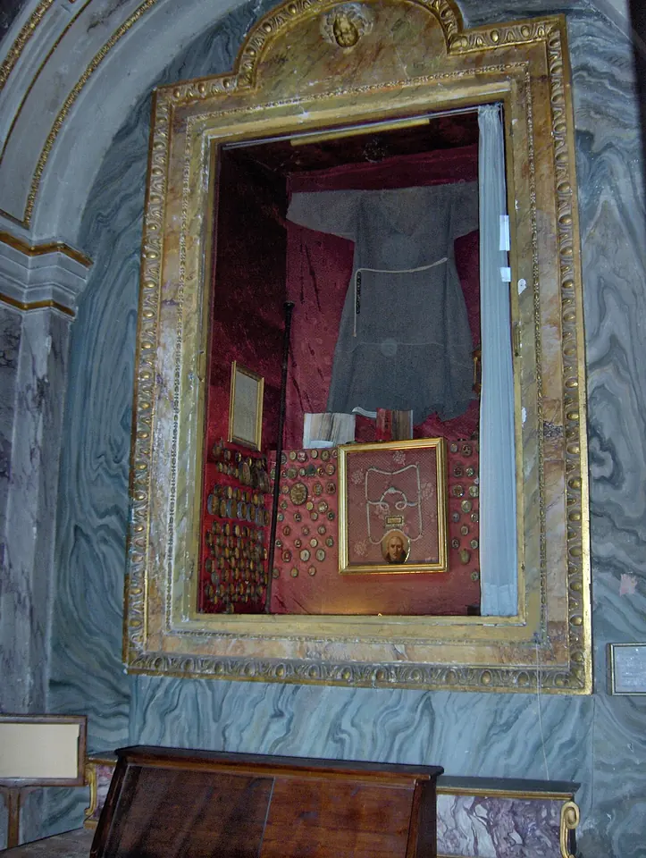 A gilded wall case in an Assisi church displaying a brown Franciscan habit, small books and relic cases, among them the breviary of Gregory Grassi