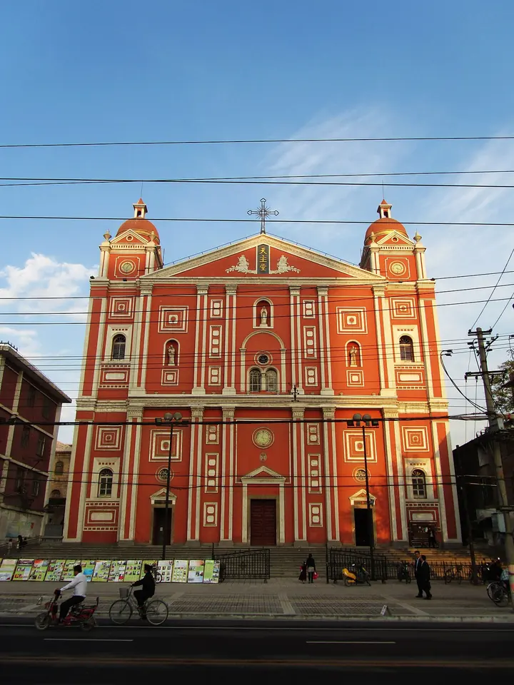 The red and white facade of the Catholic cathedral in Taiyuan, with two small domed towers and a cross, seen from a busy street