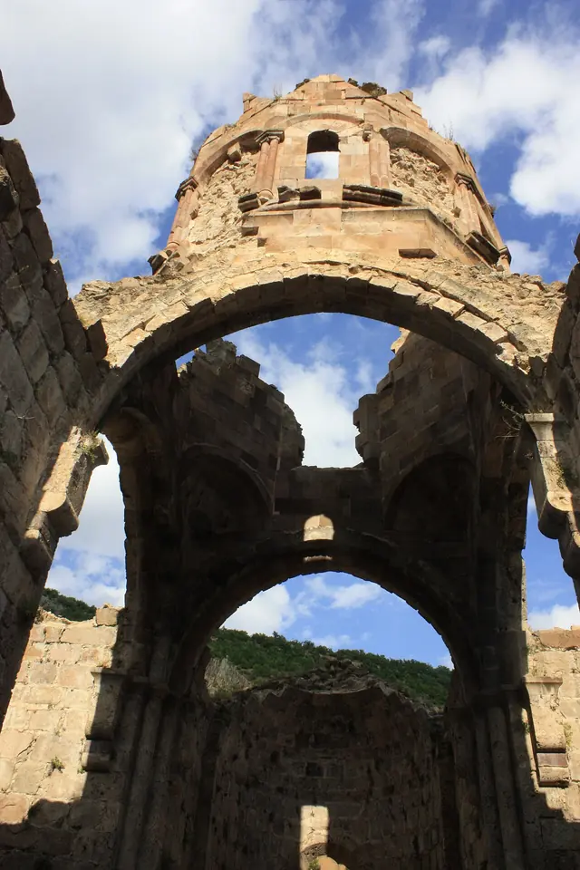 Looking up inside the roofless ruined church of Khandzta, with tall stone arches and the broken drum of the dome against a blue sky