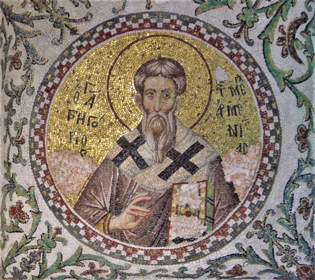 Round Byzantine mosaic medallion of St. Gregory the Illuminator with a gray beard and a halo, wearing a stole marked with black crosses and holding a book, framed by green vines