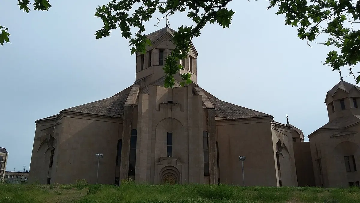 The large modern stone cathedral of St. Gregory the Illuminator in Yerevan with its conical domes, seen from a lawn under trees