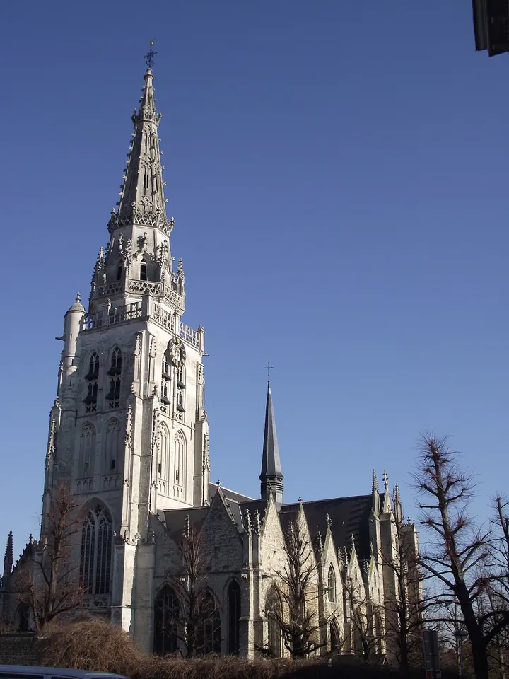 Tall Gothic church tower with a stone spire against a blue sky in Anderlecht