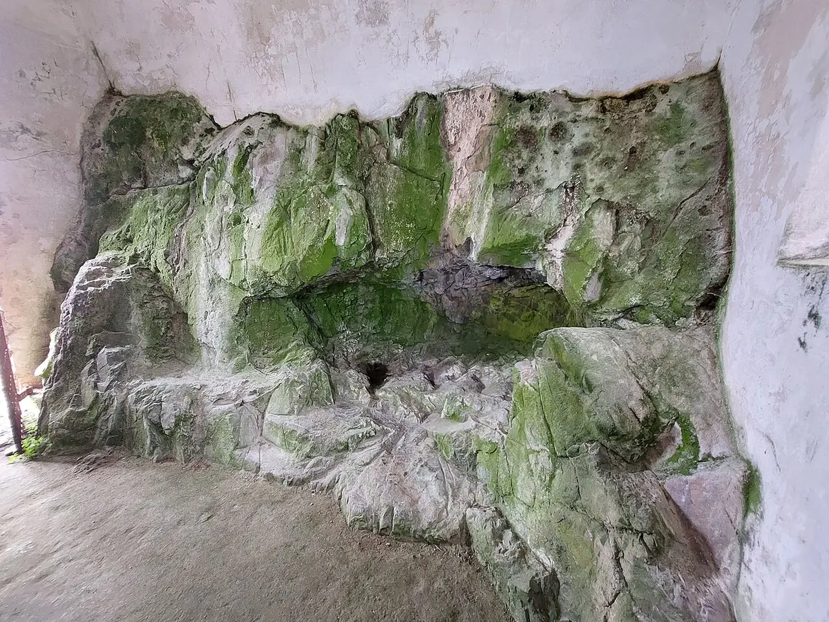 A shallow hollow in rough, lichen-green granite, enclosed by whitewashed walls inside the small Hermitage chapel