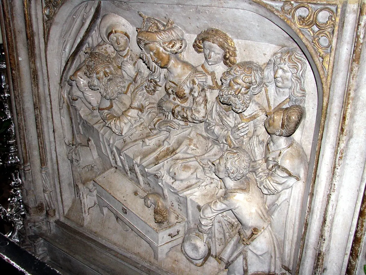 A pale stone relief of a crowned man lying ill in a canopied bed, surrounded by physicians and attendants