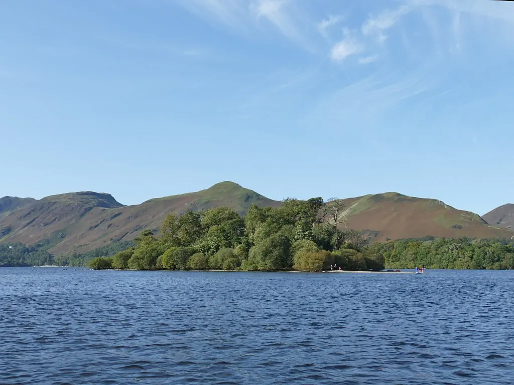 A small wooded island in a blue lake, with green and brown hills rising behind it under a clear sky