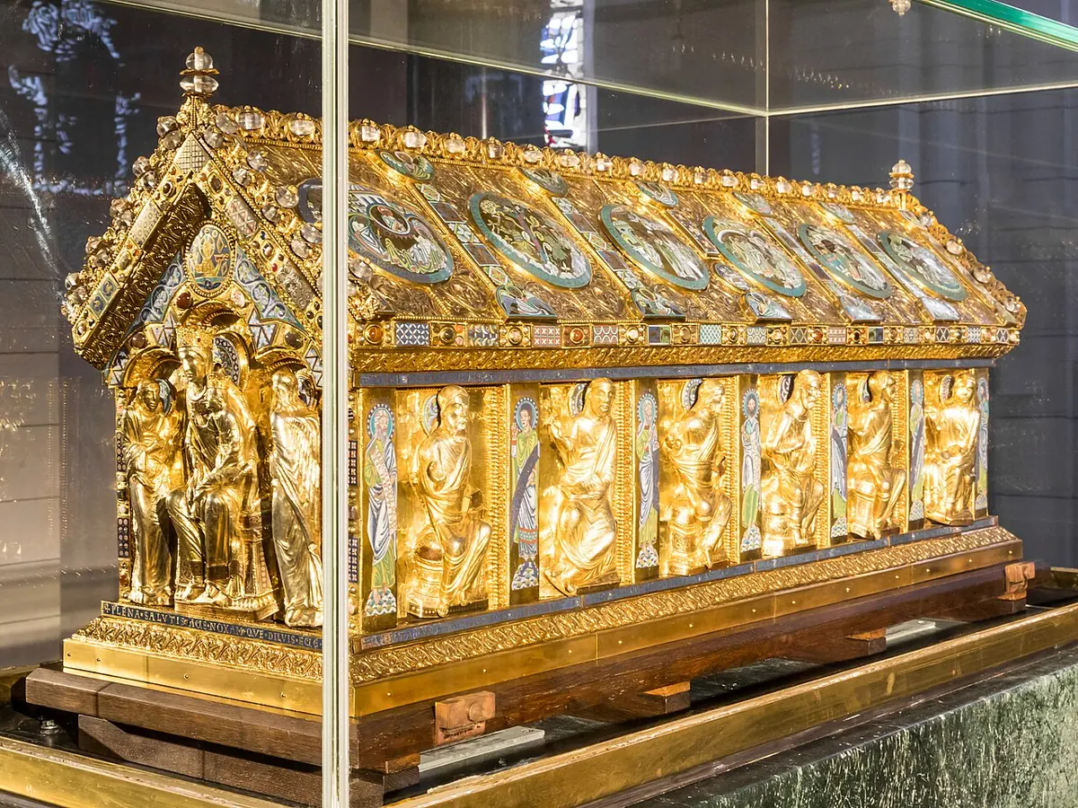 A long gilded house-shaped reliquary shrine in a glass case, its sides lined with seated figures of apostles and its roof covered with enamel medallions