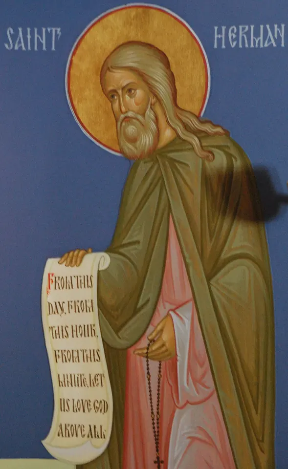 Wall icon of St. Herman in a green mantle against a blue background, holding an unrolled scroll that reads "From this day, from this hour, from this minute let us love God above all"
