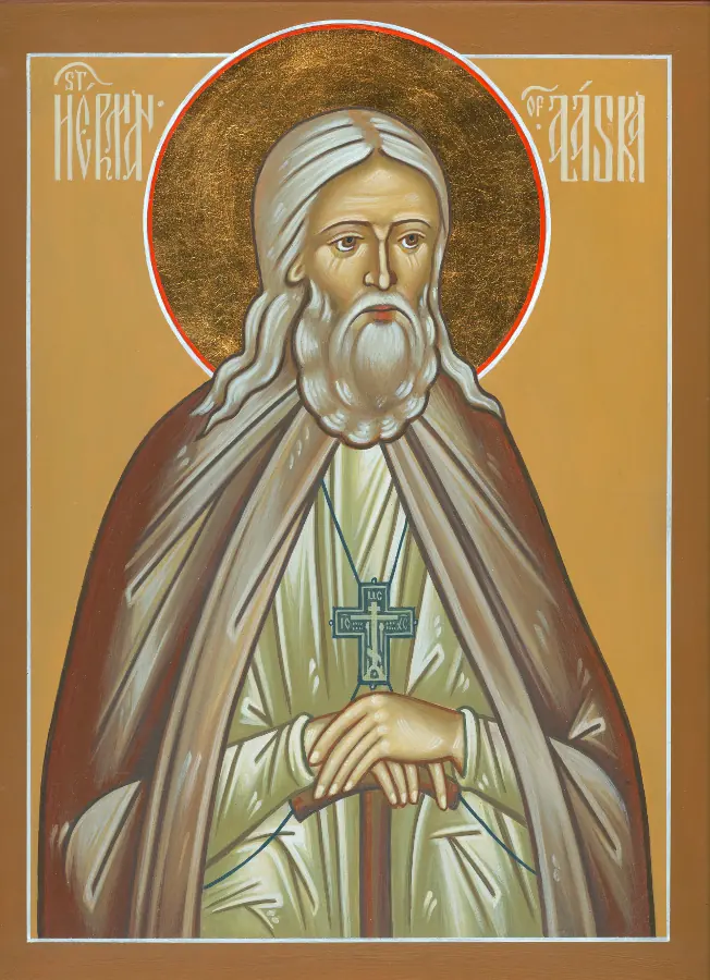 Icon of St. Herman with long white hair and beard, a dark cross on his chest and his hands crossed on a staff, against a gold background with a red-rimmed halo