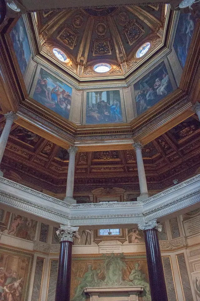 Looking up inside the octagonal Lateran Baptistery in Rome, with dark columns, a painted drum and a coffered gilded lantern above