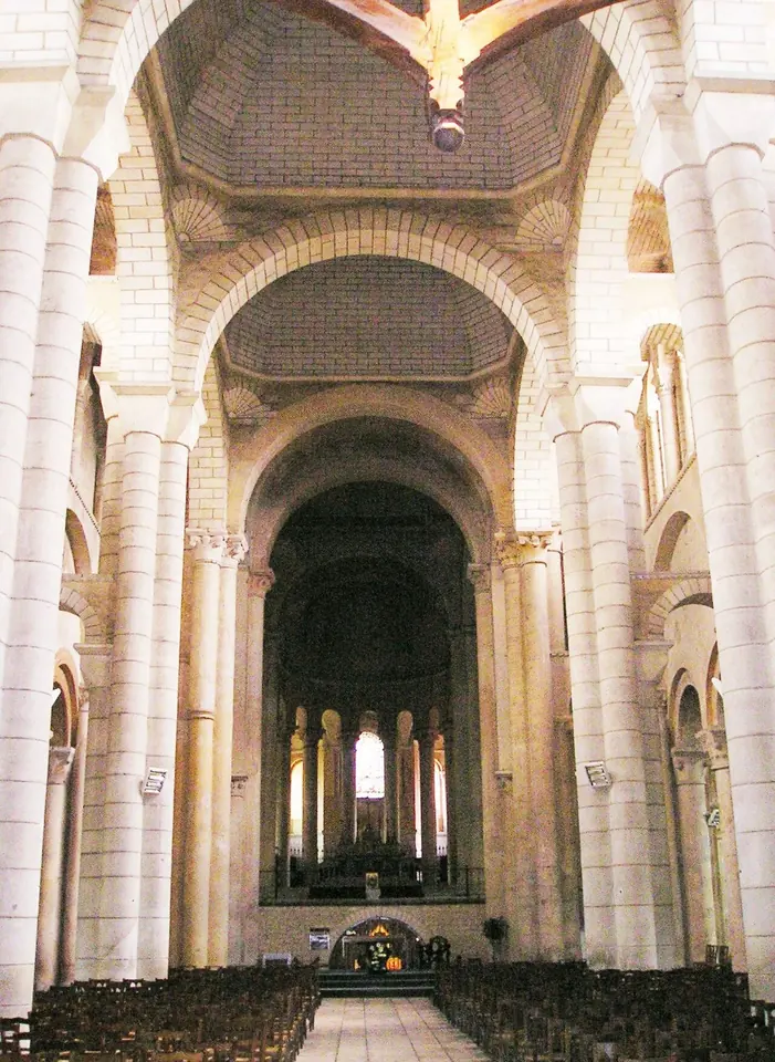 The pale stone Romanesque nave of Saint-Hilaire-le-Grand, with tall round columns and arches leading to a raised choir